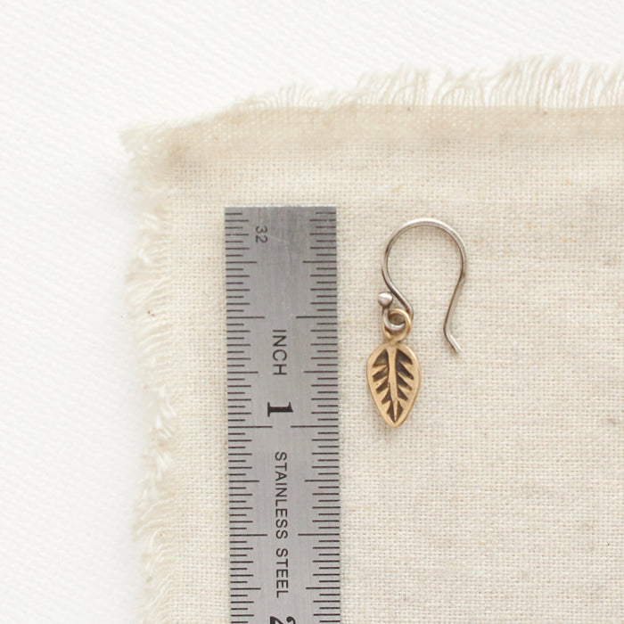 A bronze leaf earring next to a ruler for size reference