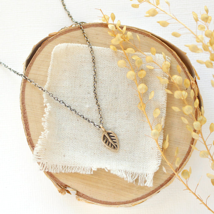 The bronze leaf necklace styled on wood with linen and dried grass