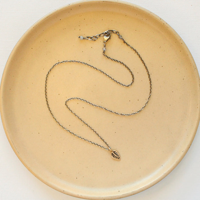 The bronze leaf necklace styled on a tan plate to show the adjustable lobster clasp closure