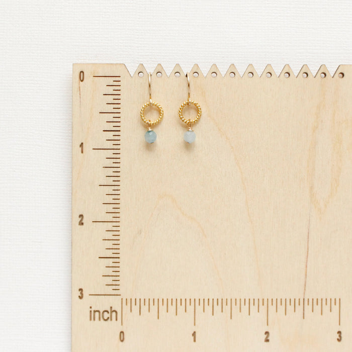 The little aquamarine gold hoop earring styled on a wooden ruler