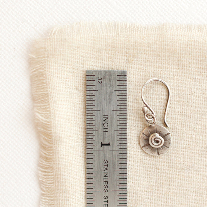 A little musana earring next to a ruler for size reference