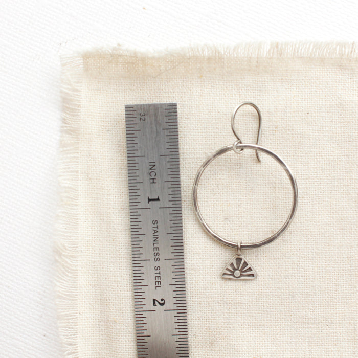 A sun rise hoop earring next to a ruler for size reference