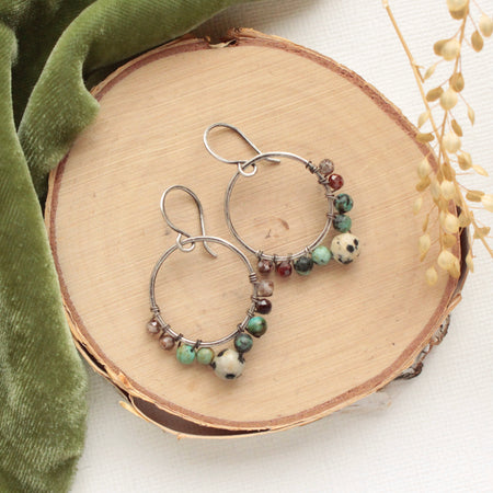 The lona hoop earrings styled on wood with green velvet and dried grass