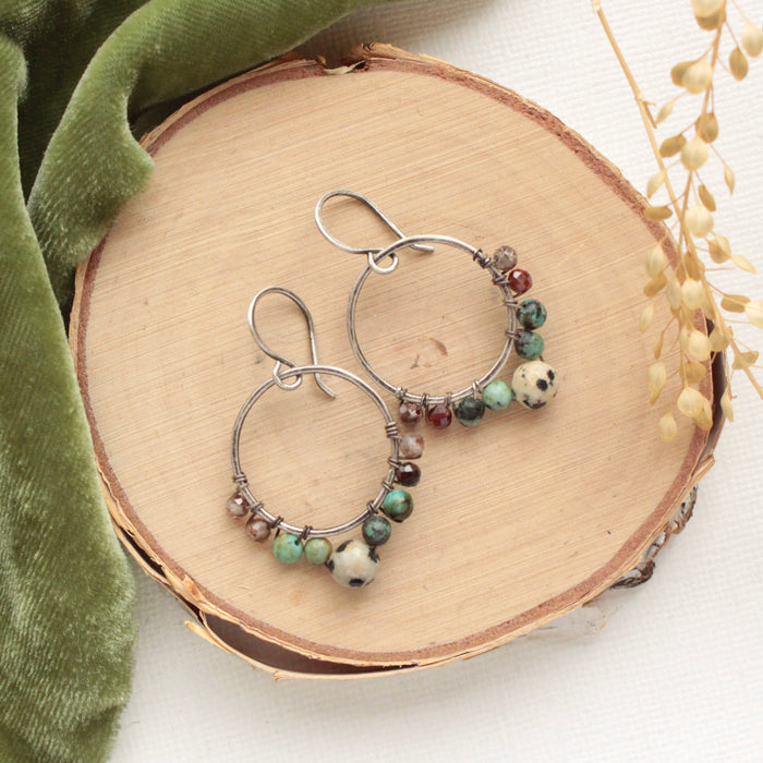 The lona hoop earrings styled on wood with green velvet and dried grass