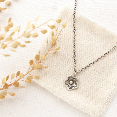 The mini cactus flower necklace styled on tan linen with dried grass