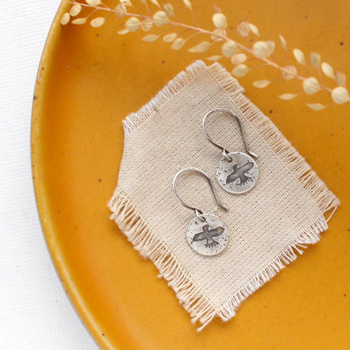 The mini soar earrings styled on a yellow plate with linen and dried grass