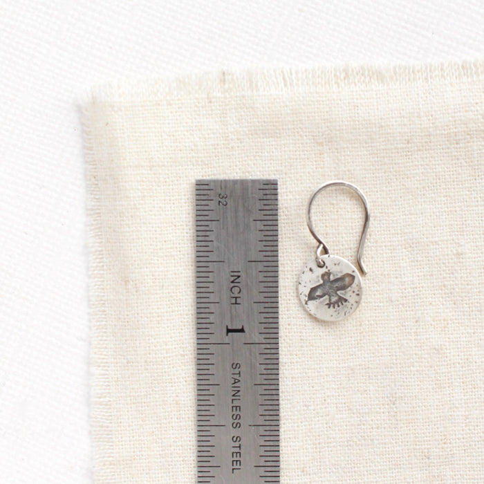 A mini soar earring next to a ruler for size reference