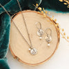 The mini sprout pearl charm necklace styled on wood with the matching earrings and blue velvet