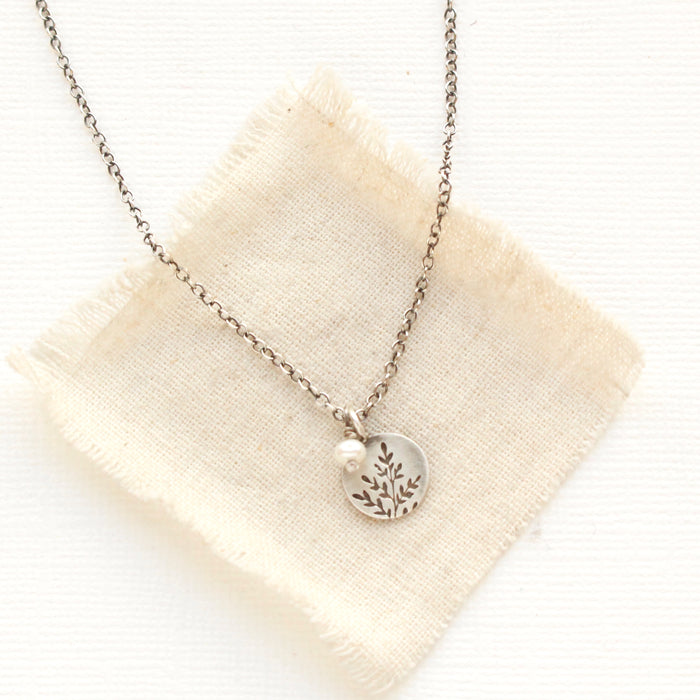 The mini sprout pearl charm necklace styled on tan linen