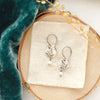 The mini sprout pearl dangle earrings styled on wood with blue velvet, linen, and dried grass