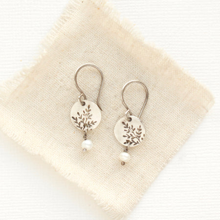 The mini sprout pearl dangle earrings styled on tan linen