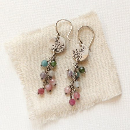 The mini sprout rainbow tourmaline earrings styled on tan linen