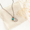 The mini sprout turquoise charm necklace styled on tan linen with dried grass