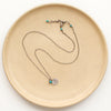 The mini sprout turquoise charm necklace styled on a tan plate to show the adjustable lobster clasp closure