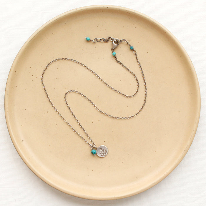 The mini sprout turquoise charm necklace styled on a tan plate to show the adjustable lobster clasp closure