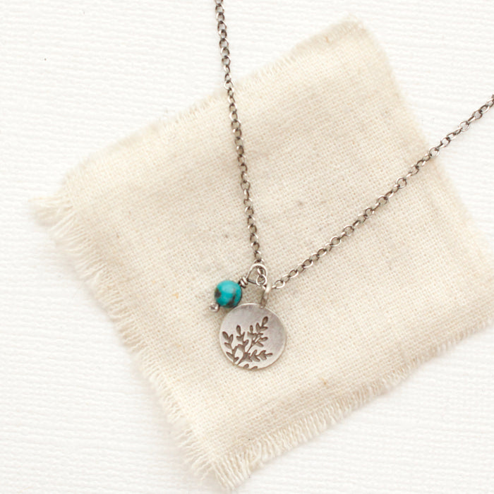 The mini sprout turquoise charm necklace styled on tan linen