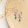 The mini sprout turquoise dangle earrings styled on a tan plate with dried grass