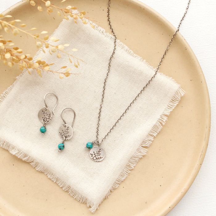 The mini sprout turquoise dangle earrings styled on a tan plate with the matching necklace