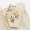 The mini talara shield earrings styled on a tan rock with linen and dried grass