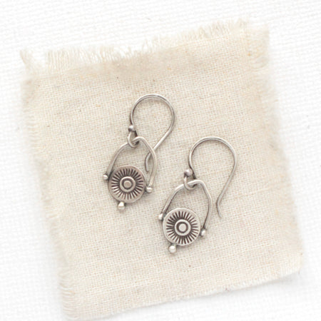 The mini talara shield earrings styled on tan linen