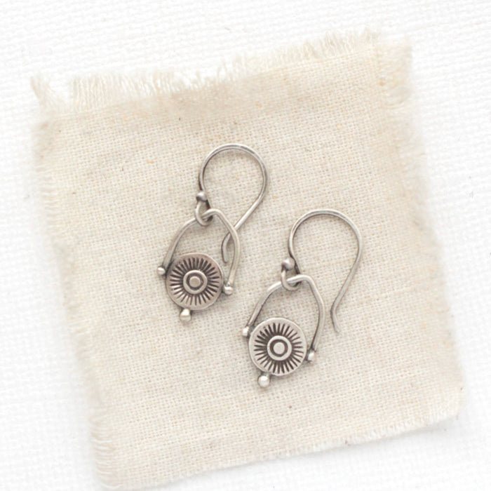 The mini talara shield earrings styled on tan linen