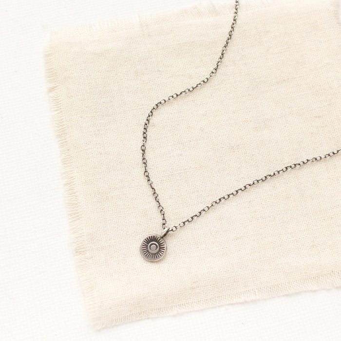 The mini talara sun necklace styled on tan linen