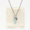 The larimar, pearl, and kyanite charm necklace styled on tan linen.