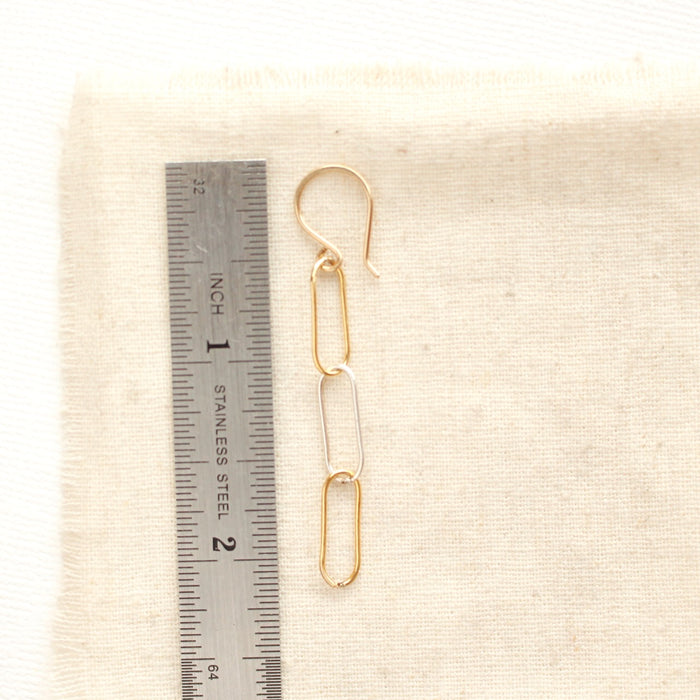A mixed metal paperclip earring next to a ruler for size reference