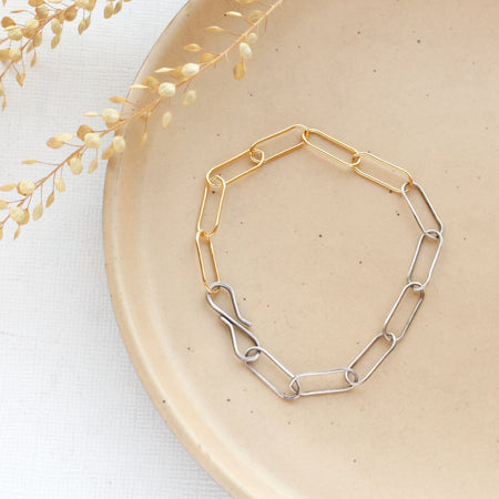The mixed metal paperclip bracelet styled on a tan plate with dried grass