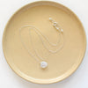 The silver moonstone drop necklace styled on a tan plate to show the adjustable lobster clasp closure