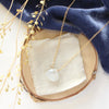 The gold moonstone drop necklace styled on wood with blue velvet and dried grass