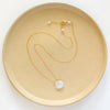 The gold moonstone drop necklace styled on a tan plate to show the adjustable lobster clasp closure