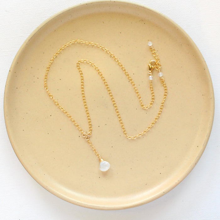 The moonstone gold lariat necklace styled on a tan plate to show the adjustable lobster clasp closure