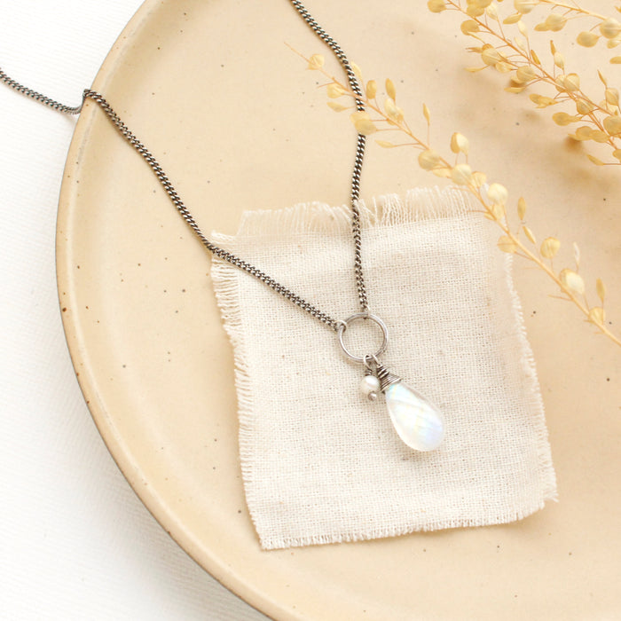 The moonstone and pearl necklace styled on a tan plate with linen and dried grass