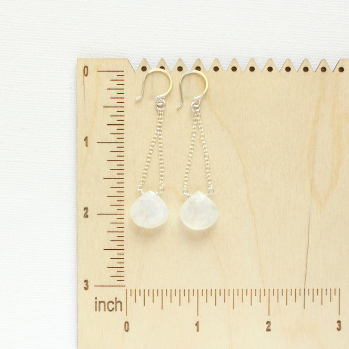 The moonstone swing earrings on a wooden ruler for size reference