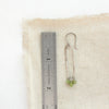 An olivine jade forged long hoop earring styled next to a ruler for size reference