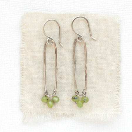 The olivine jade wrapped long forged hoop earrings styled on tan linen