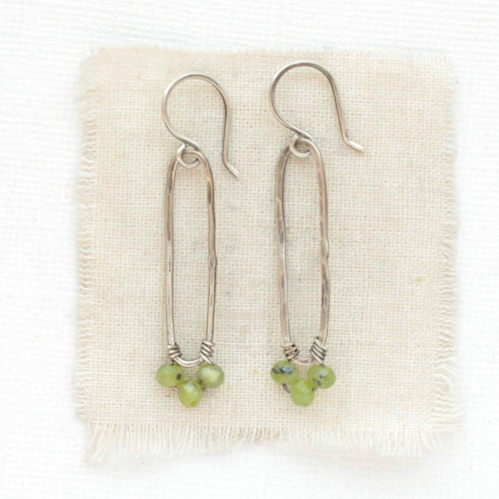The olivine jade wrapped long forged hoop earrings styled on tan linen