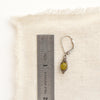 A olivine jade wrapped earring next to a ruler for size reference