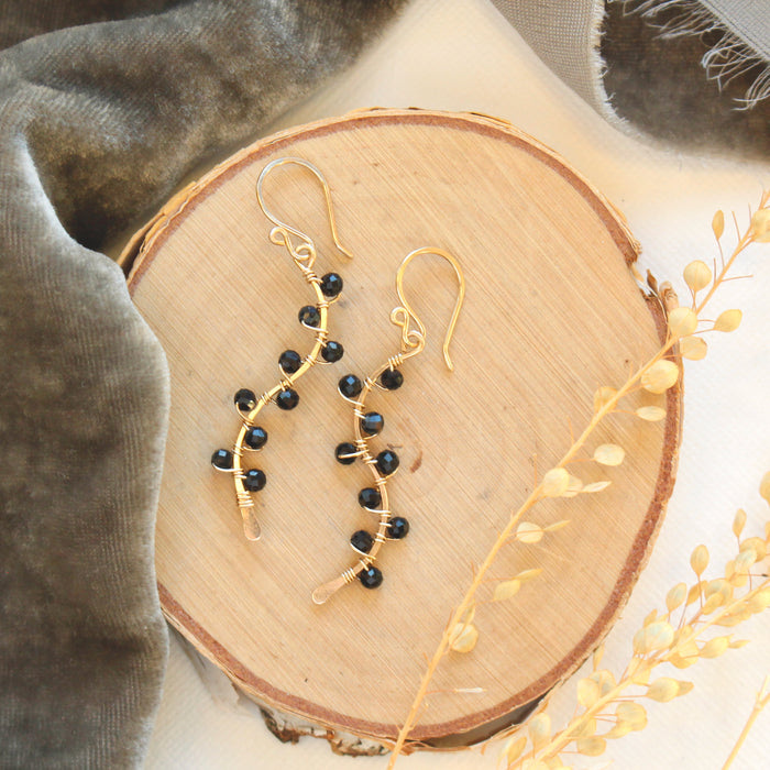 The onyx wrapped gold vine earrings styled on wood with gray velvet and dried grass