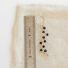 A onyx wrapped gold vine earring next to a ruler for size reference
