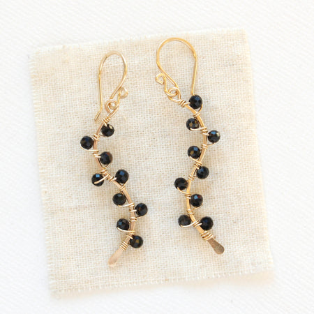 The onyx wrapped gold vine earrings styled on tan linen
