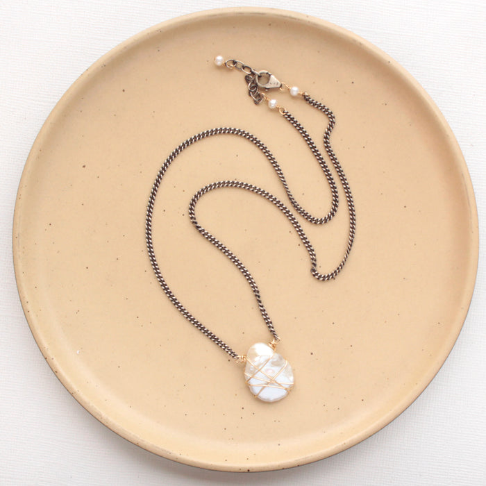 The organic pearl mixed metal necklace styled on a tan plate to show the adjustable lobster clasp closure