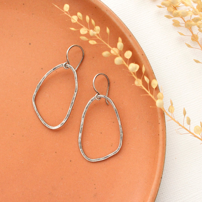 The organic silver hoop earrings styled on an orange plate with dried grass