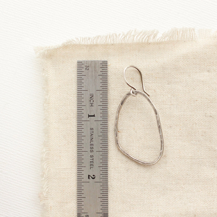 An organic silver hoop earring next to a ruler for size reference