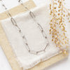 The oxidized silver paperclip necklace styled on a tan rock with linen and dried grass