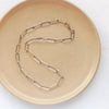 The oxidized silver paperclip necklace styled on a tan plate to show the whole chain