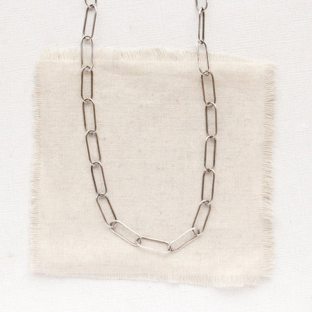 The oxidized silver paperclip necklace styled on tan linen