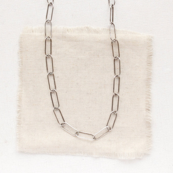 The oxidized silver paperclip necklace styled on tan linen