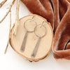 The pakal long triangle hoop earrings styled on wood with orange velvet and a stick